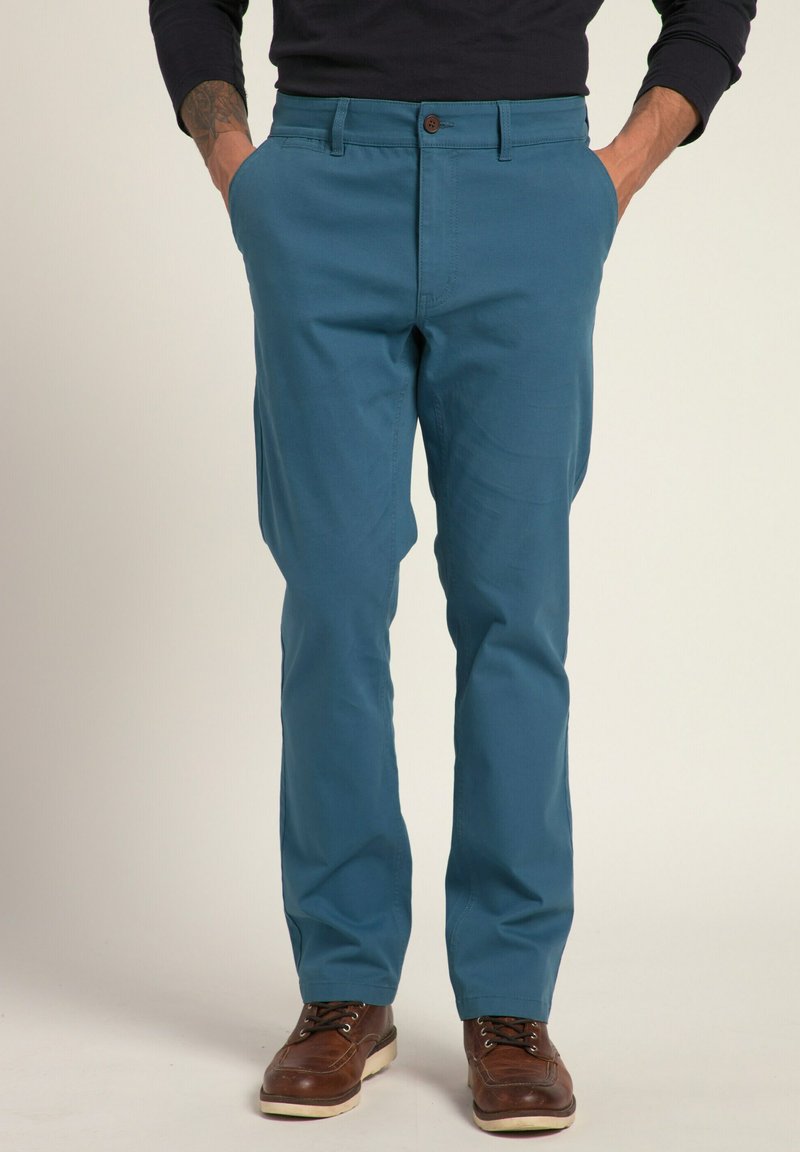 Tyrkysové bavlněné kalhoty s rovnou nohavicí, s bočními kapsami a zapínáním na knoflík vpředu, spojené s hnědými šněrovacími botami.