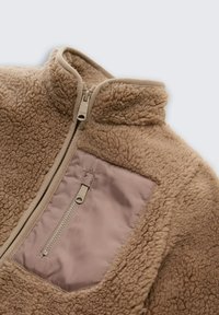 Beige fleecejack met een hoge kraag, ritssluiting en een contrasterende mauve zak. Zachte textuur en een gezellige, warme uitstraling.