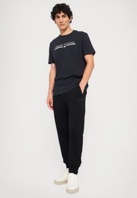 Svart bomull T-skjorte med hvit "Armani Exchange" logo, kombinert med svarte joggebukser med matchende logodetalj og hvite sneakers.
