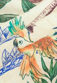 Bomuldsstof med farverige papegøjer i orange, grøn og blå, præget af detaljerede blade og botaniske illustrationer.