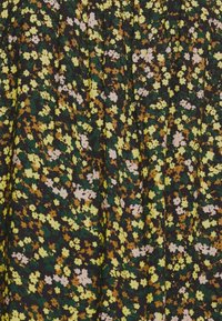 Tissu foncé avec un motif floral dense et petit en jaune, marron, vert et rose pâle, montrant des plis souples et une texture.