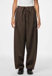 Rudos spalvos dryžuotos kelnės su plačiomis kojų apačiomis, elastinga juosmens dalis ir raištelis. Medžiaga atrodo lygi ir šiek tiek blizgi.