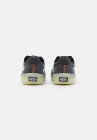 Duas sapatilhas Vans pretas com um upper de tecido texturizado, costura em vermelho contrastante e solas translúcidas com o logótipo "Off the Wall".