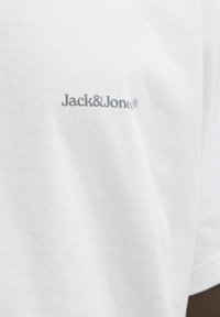 Bílý bavlněný tričko s šedým potiskem loga "Jack&Jones®" na levé části hrudi. Měkká textura s klasickým kulatým výstřihem.