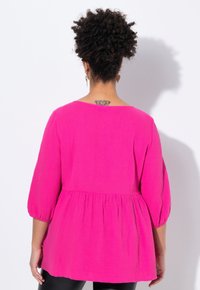 Top peplum fucsia realizzato in tessuto testurizzato, con maniche a tre quarti e scollatura ampia, caratterizzato da dettagli arricciati in vita.