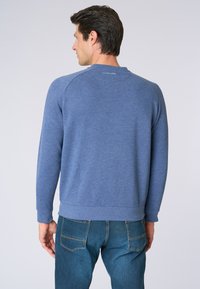 Felpa blu realizzata in morbido misto cotone, con maniche e orlo a coste, scollo tondo e un logo sottile sulla parte posteriore. Indossata con jeans.