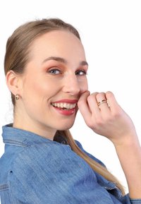 Gouden en zilveren ring met diamanten accenten, gedragen aan de hand. Model in een lichtblauwe denim blouse, lachend, met haar opgestoken. Witte achtergrond.