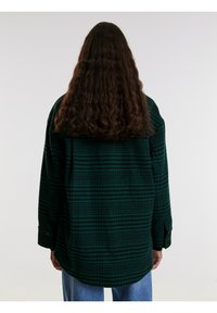 Groen en zwart geruite flanellen shirt met een ontspannen pasvorm, knoopmanchetten en een gebogen zoom, gezien van achteren. Beschikt over een gestructureerde stof.