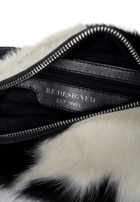 Interno di una borsa in finta pelliccia bianco e nero con una cerniera elegante, dettagli in pelle e un'etichetta che recita "RE DESIGNED EST. 2003."