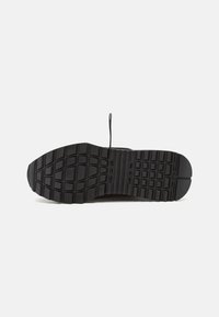 Baskets noires avec une semelle en caoutchouc texturée. Elles possèdent des rainures profondes pour une meilleure adhérence et une languette en boucle au talon pour faciliter l'enfilage.