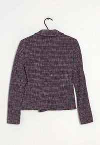 Tkaninowy żakiet w granatowym kolorze z czerwonymi i białymi flekami, z długimi rękawami i klapami. Widok z tyłu pokazuje dopasowany krój i wykończenie.