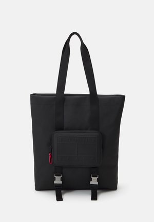 Schwarze Tote-Bag mit langen Henkeln, frontseitigem Reißverschlussfach mit geprägtem Text und zwei silbernen Schnallenriemen am Boden.