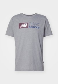 Szara bawełniana koszulka z krótkim rękawem, okrągłym dekoltem, z wyróżniającym się logo "New Balance" w ciemnofioletowym i niebieskim na przodzie.