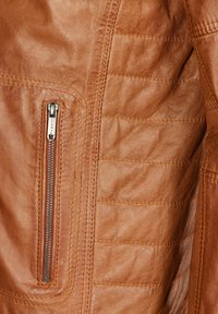 Detalles de una chaqueta de cuero marrón con un acabado texturizado, que presenta un bolsillo con cremallera vertical y paneles bordados en horizontal.