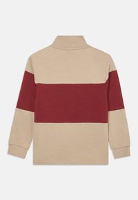 Langærmet polo-shirt med en beige krop og en vandret maroon stribe hen over brystet, med en foldet krave og ribbede manchetter.