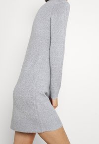 Grå stickad klänning med långa ärmar, ribbade muddar och en lätt avsmalnande nederkant. Mjuk textur och medellängd.