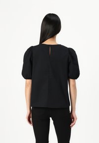 Svart bluse med pufferm, rund halsutskjæring og et nøkkelhullåpning bak. Laget av glatt stoff, designet med en løs passform.
