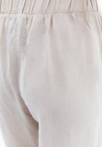Pantalons en lin beige clair avec un tissu texturé et légèrement froissé. Dotés d'une taille élastique pour plus de confort et d'un design ample et fuselé.