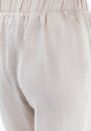 Pantalones de lino color beige claro con una tela texturizada y ligeramente arrugada. Presentan una cintura elástica para mayor comodidad y un diseño suelto y ajustado.