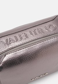 Fialová kožená kapsa s metalickým efektem, s vyraženým logem "VALENTINO" a stříbrným zipem. Povrch s texturou a elegantním designem.
