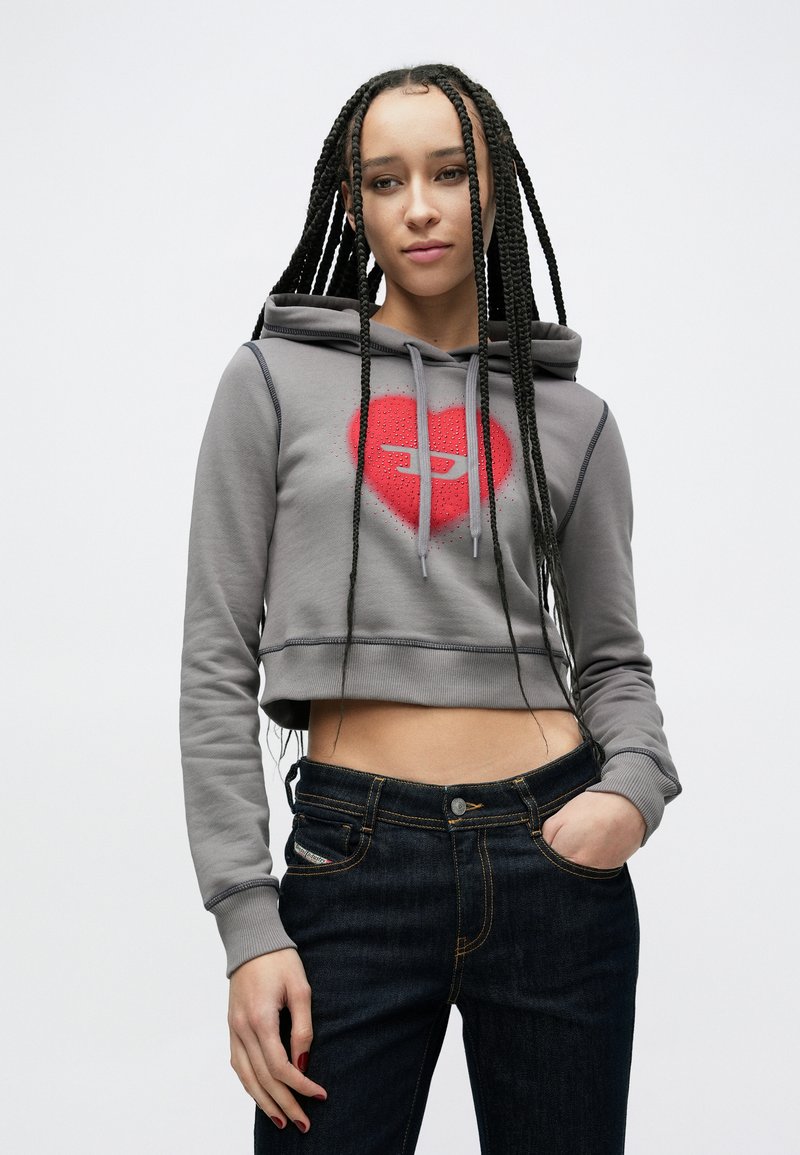 Grey cropped hoodie with a red heart graphic on the front, adjustable drawstrings, and ribbed cuffs, paired with dark blue denim jeans.
