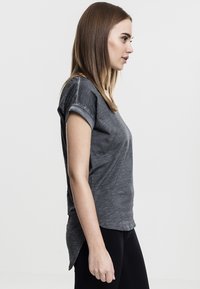 Šedé tričko s krátkým rukávem, s ohrnutými manžetami, volný střih a zaoblený lem. Vyrobeno z měkkého materiálu s mírně texturovaným povrchem.
