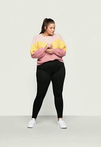 Sweater listrado rosa e amarelo de mangas longas, combinado com leggings pretas e ténis brancos, sobre um fundo claro.