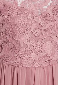 Różowa sukienka z misternym haftem kwiatów i liści na przezroczystym korpusie, z falującą, warstwową spódnicą z szyfonu poniżej.