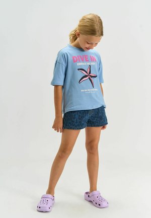 Light blue t-shirt with a pink starfish graphic and text, paired with navy leopard-print shorts and lavender clogs. Casual summer outfit.