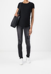 Mustat ribbattuja lyhythihaiset paita, harmaat revityt skinny-farkut ja valkoiset tennarit. Musta käsilaukku, jossa on pitkä hihna, pidetään vasemmassa kädessä.