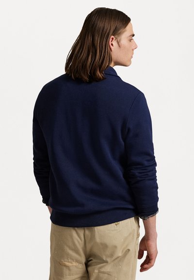 Temno modra majica s krožnim izrezom, rebrastimi manšetami in robom. Tkanina se zdi mehka in teksturirana, z sproščenim krojem.