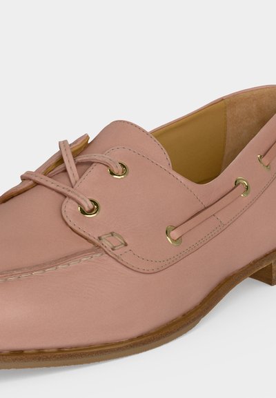 Ροζ δερμάτινο μοκασίνι με χρυσά κορδόνια, δεμένα κορδόνια, ραφές και ανοιχτό καφέ σόλα σε λευκό φόντο.