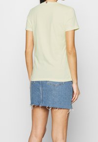 Helles gelbes kurzärmliges T-Shirt mit Rundhalsausschnitt, kombiniert mit einem blauen Jeans-Minirock, der einen ausgefransten Saum und Gesäßtaschen hat.