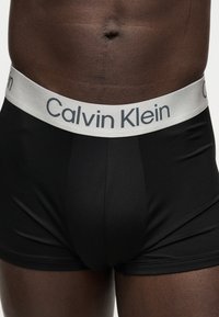 Άνδρας με μαύρα μπόξερ Calvin Klein, με λευκή μέση και εμφανές λογότυπο της μάρκας.