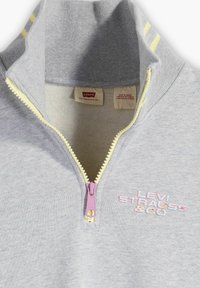 Sudadera gris con cuello con media cremallera, detalles en amarillo y logo bordado en rosa y azul. Presenta una cremallera ligera y una textura de mezcla de algodón.
