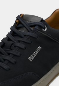 Sapatilha de couro azul-escuro com bico redondo, atacadores planos e sola de borracha bege. Apresenta olograma "Blauer" em relevo e costura em contraste.