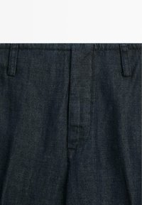 Tmavě modré džíny s poutky na pásek a viditelným předním zapínáním na zip, zobrazené zblízka.