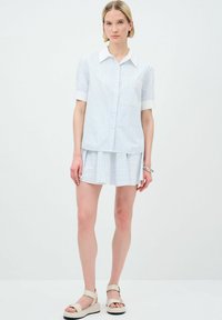 Camicia a maniche corte a righe blu chiaro e bianche con bottoni sul davanti, colletto e taschino sul petto, abbinata a una gonna svasata.
