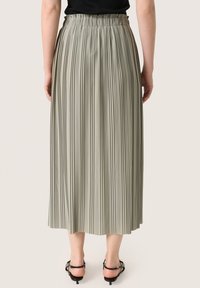 Lichtgroene geplooide midi rok met een elastische tailleband, met verticale plooien en een gladde textuur, gecombineerd met zwarte sandaaltjes met bandjes.