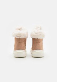 Botas tobilleras de ante marrón con un suave cuello de piel sintética color crema y suelas de goma blancas. Logo de Geox visible en la parte trasera.