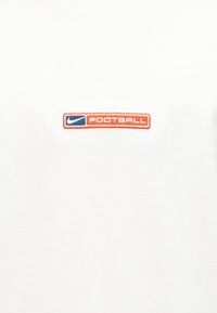 Biele tkanina s malou obdĺžnikovou náplasťou s logom Nike vedľa slova "FUTBAL" v oranžovej a modrej farbe.