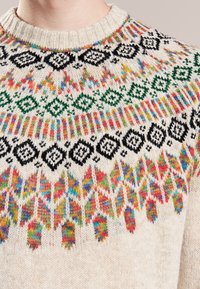 Kremový pletený svetr s barevným geometrickým vzorem na yokě v černé, zelené a živých odstínech. Hribkovaný výstřih a texturovaný povrch.
