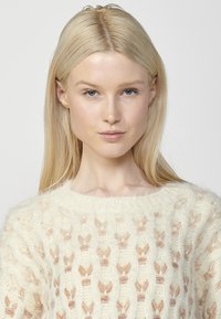 Pulover tricotat în nuanță crem, cu o textură moale, având un model format din fluturi mici de culoare maroniu deschis pe întreaga suprafață. Gât rotund cu margine ribbatată.
