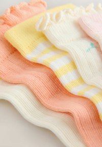 Pila de suaves calcetines para bebé con textura acanalada en colores pastel, que incluyen blanco, durazno, rayas amarillas y un par con bordes fruncidos.