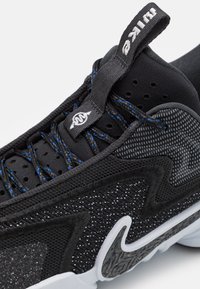 Baskets noires avec une tige en mesh, des accents texturés, des lacets bleus et une semelle extérieure blanche avec un motif de crampons noirs distinctif.