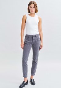 Grijze corduroy broek met een slim fit, zijzakken en knoopsluiting, gecombineerd met een witte mouwloze top en zwarte loafers.