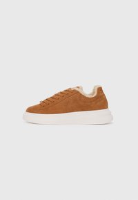 Brown suede sneaker with white rubber sole, rounded toe, lace-up design, and soft, fur-like interior lining. Features a textured surface.