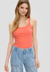 Korallenfarbener, gerippter Tanktop mit breiten Trägern, kombiniert mit hellblauen, hoch taillierten Jeansshorts mit Knopfleiste und Seitentaschen.