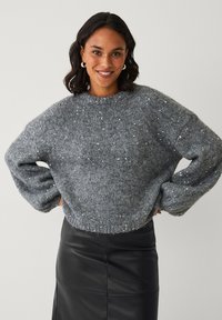 Grauer, gestrickter Pullover mit rundem Ausschnitt, durchsetzt mit silbernen Pailletten. Verfügt über lockere Ärmel und eine entspannte Passform. Kombiniert mit einem schwarzen Lederrock.