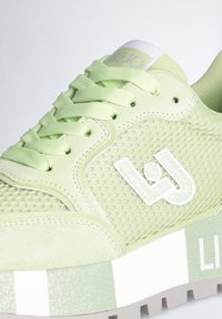 Sneaker verde chiaro con texture in suede e mesh, punta tonda, suola spessa con un motivo a strisce glitterato e dettaglio del logo in rilievo.